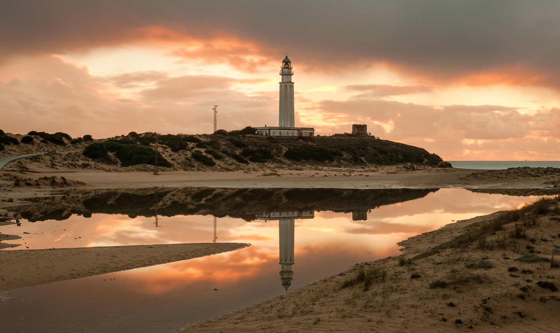 El Faro de Trafalgar reflejado sobre la arena mojada al atardecer, en Los Caños de Meca, Cádiz